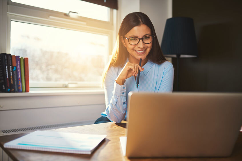 Business woman working at office looking at laptop with a pen in her hand