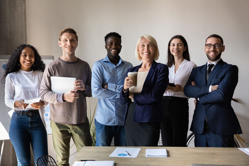 Happy confident diverse old and young business people stand together in office, smiling multiethnic professional colleagues staff group look at camera, human resource concept, team corporate portrait